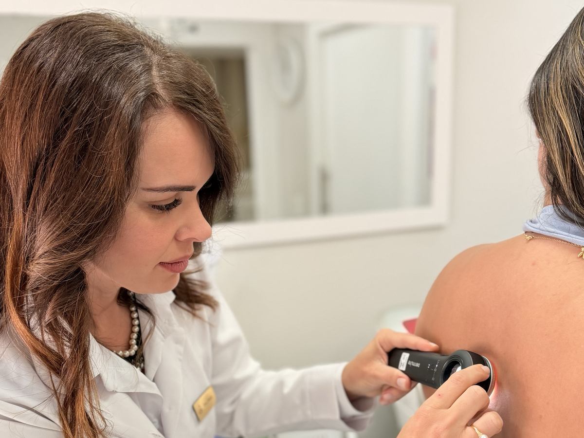 Dra. Paula Carvalho examinando a pele de uma paciente com dermatoscópio, no consultório da Clínica Evoluto